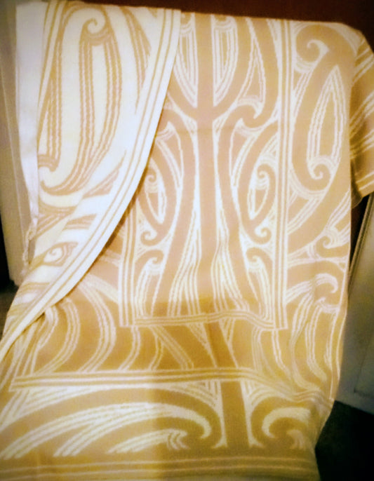 Close-up of a beige and white maori-pattern organic cotton blanket.