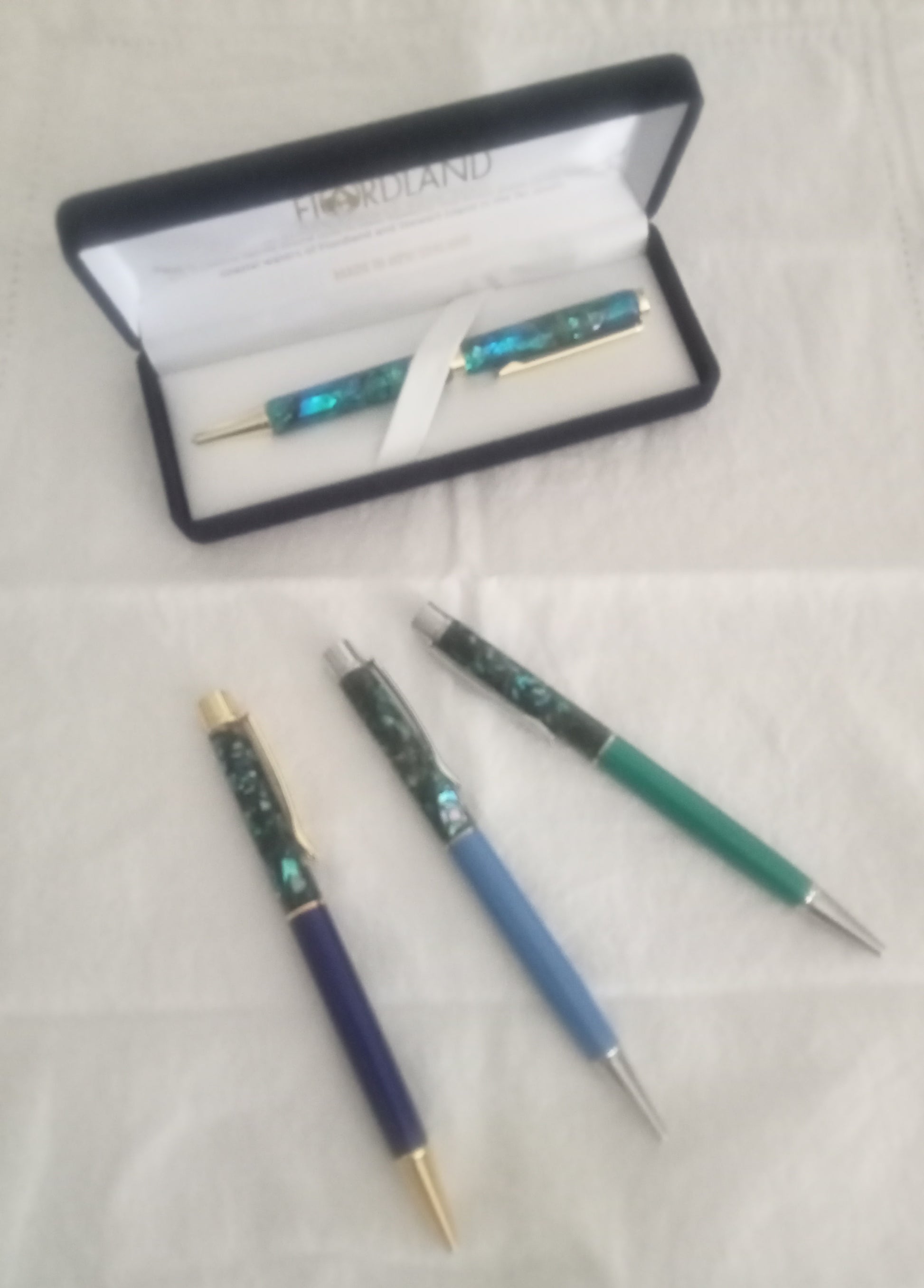 Set of three paua pens, different colours with another paua pen in branded case on a light background