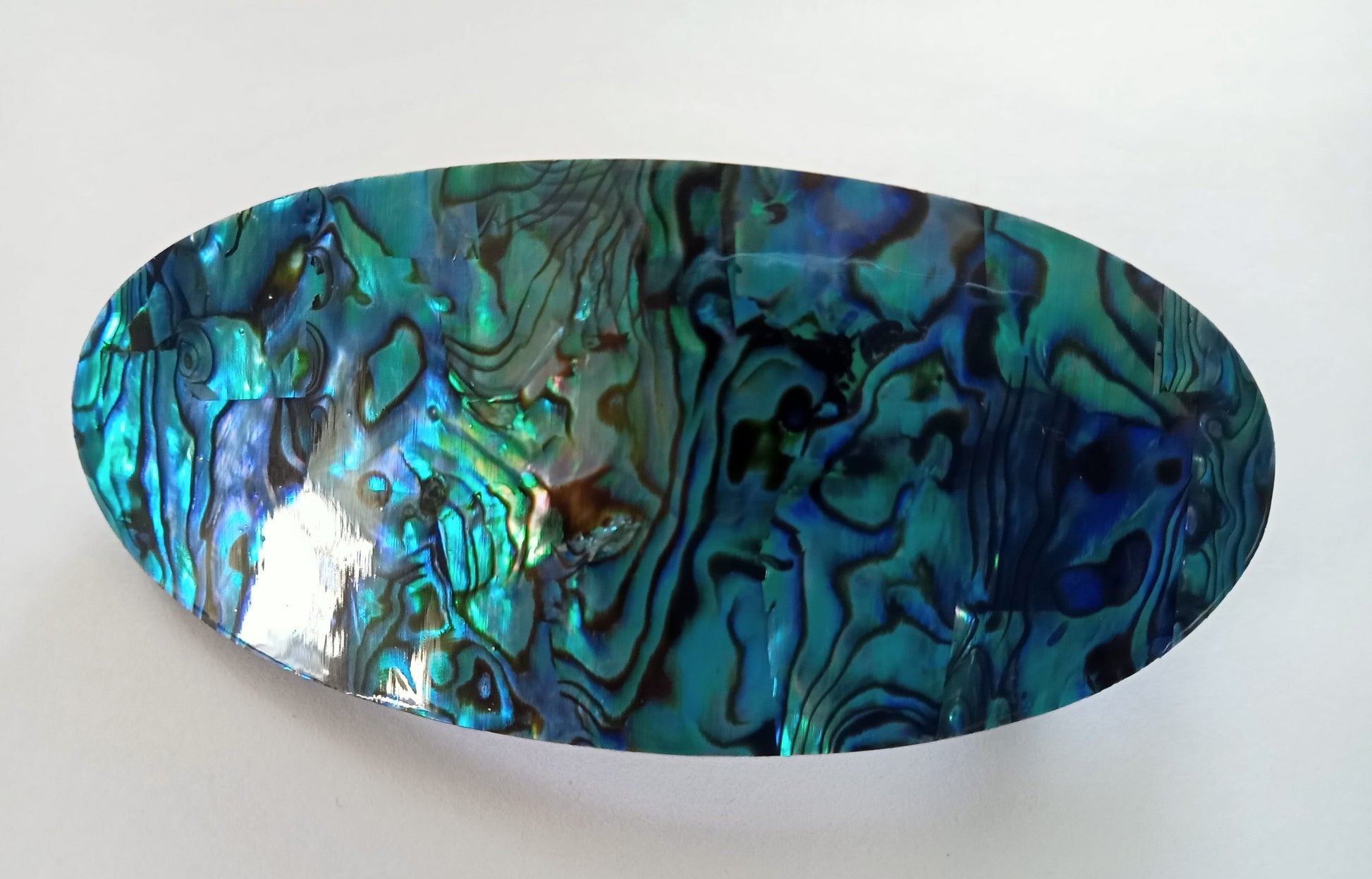eliptical shape of paua  clasp on white background, highlights beauty emanating from the shell.