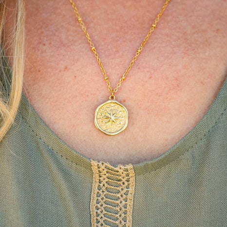 Gold necklace with a pendant worn by a person in a green top.