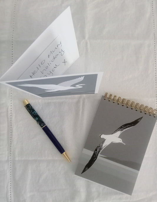 Notebook, pen, and card with bird design on a textured white surface