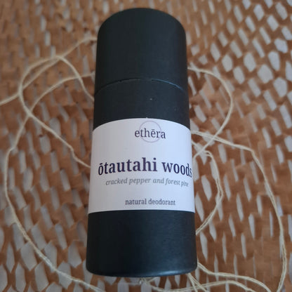 A black cylindrical deodorant stick with a white label reading 'ethéra ōtautahi woods cracked pepper and pine peat natural deodorant', placed on a woven brown surface with string.