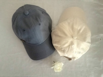 Two baseball caps, one gray and one beige, on a light surface.