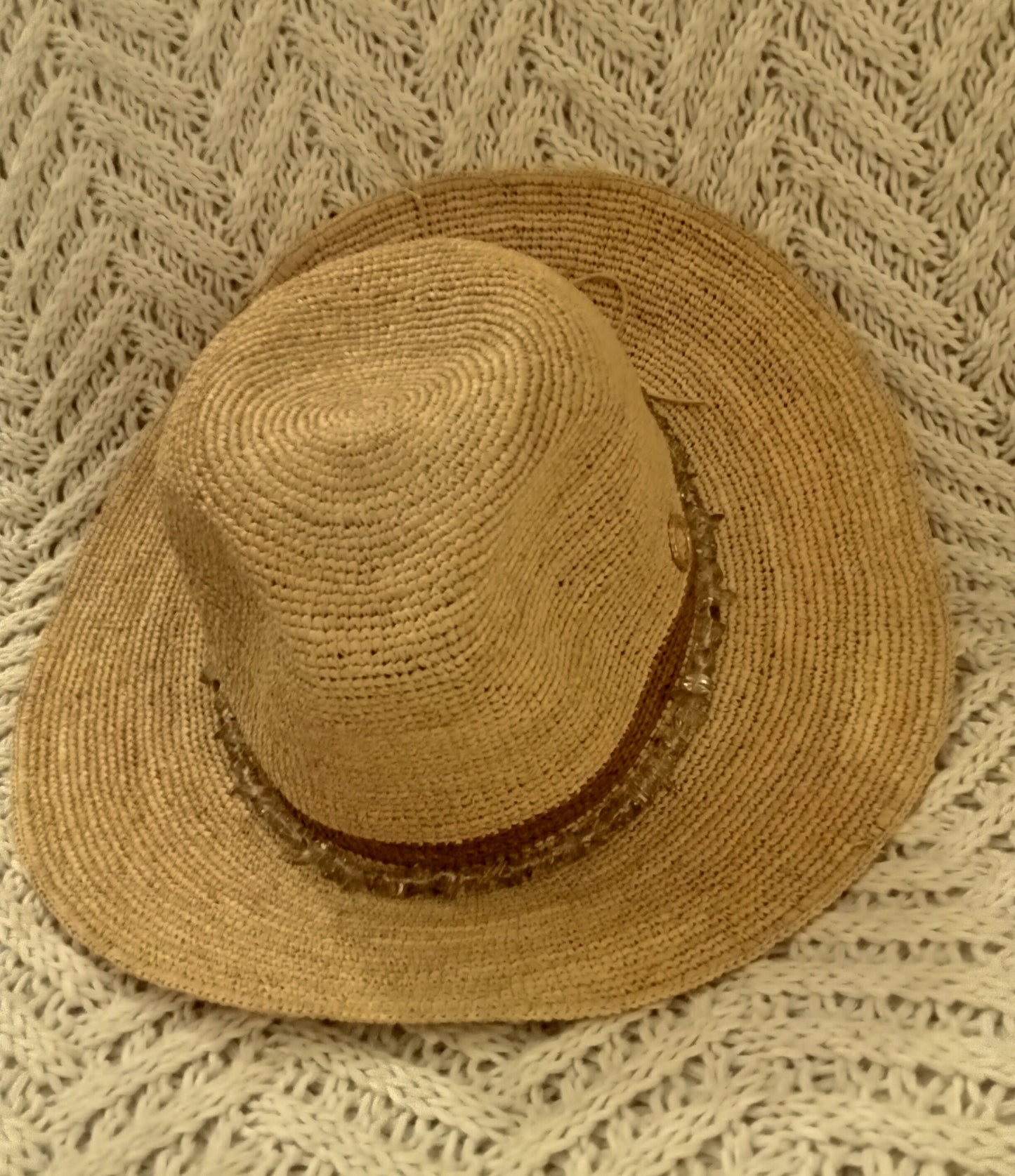 Brown straw hat with brown band and beads on a textured beige blanket.